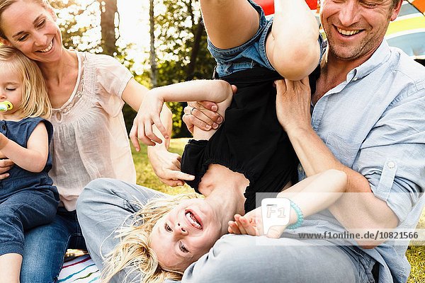 Father turning daughter upside down at family picnic in park