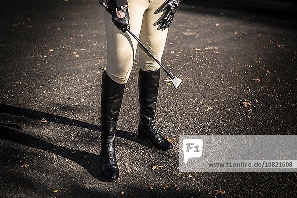 Woman wearing riding boots  holding riding crop  low section