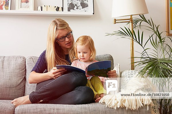 Mittlere erwachsene Frau und Kleinkind Tochter beim Lesen auf dem Sofa