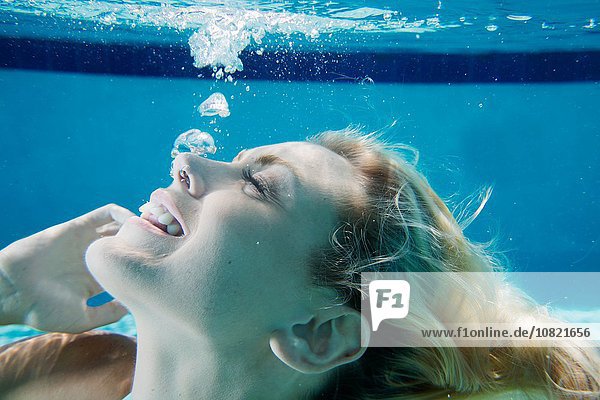 Cropped underwater view of young woman in swimming pool  releasing bubbles from mouth looking up smiling