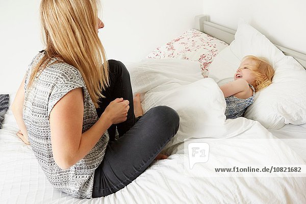 Mittlere erwachsene Frau auf dem Bett sitzend mit Kleinkind-Tochter vor dem Schlafengehen