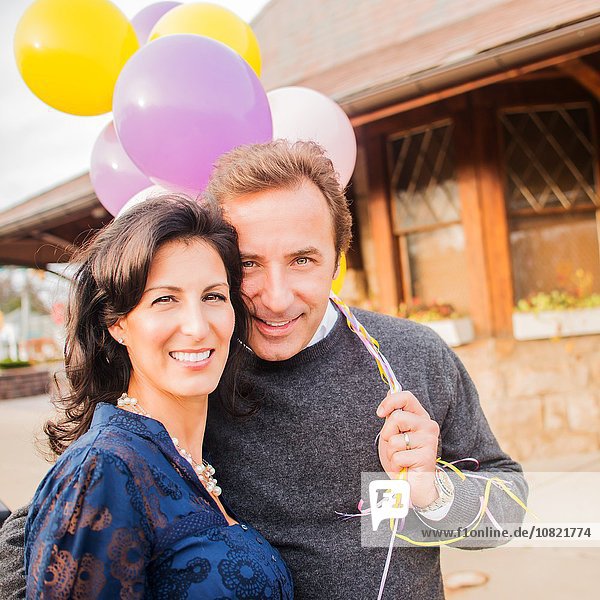 Porträt eines erwachsenen Paares,  lächelnd,  mit Luftballons im Arm