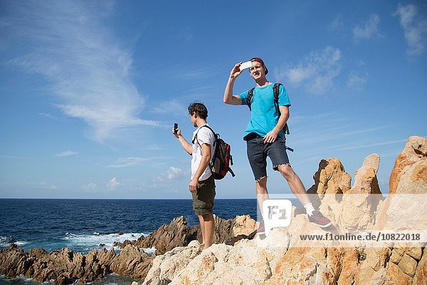 Junge Männer auf Felsen stehend mit dem Smartphone fotografieren  Costa Paradiso  Sardinien  Italien