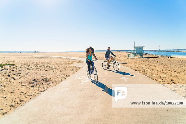 Couple cycling along pathway at beach
