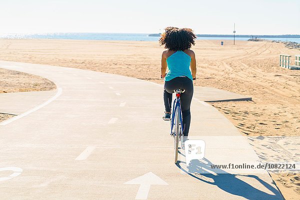 Mid adult woman cycling on pathway at beach  rear view