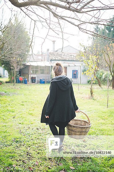 Durchgehende Rückansicht der jungen Frau im Garten mit Weidenkorb