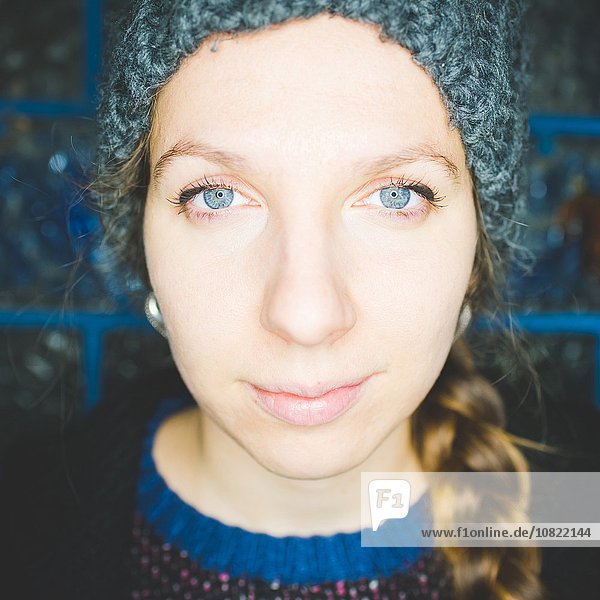 Close up portrait of young woman with plaited hair wearing knit hat looking at camera smiling