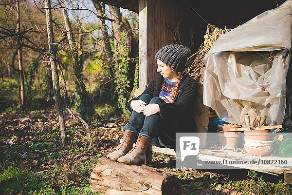 Young woman sitting in storage shed wearing knit hat looking away