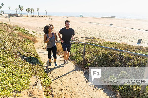 Couple running along pathway by beach