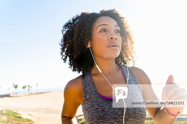 Mid adult woman running by beach  wearing earphones