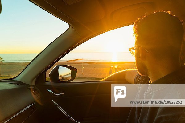 Junger Mann schaut bei Sonnenuntergang aus dem Autofenster