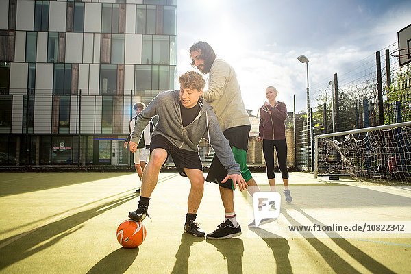 Group of adults playing football on urban football pitch
