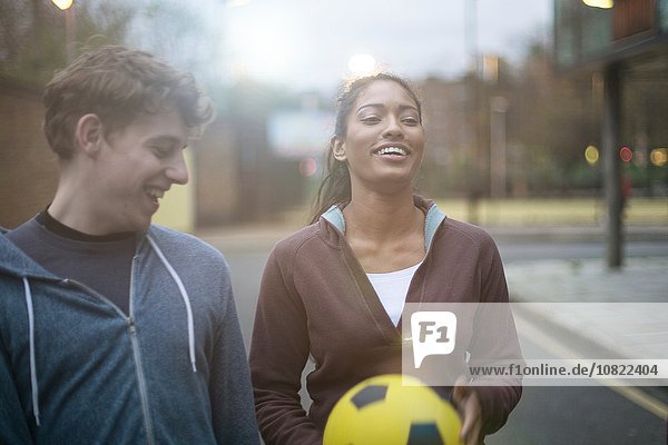 Junger Mann und junge Frau  die auf der Straße gehen und Fußball halten