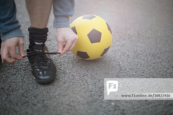 Junger Mann mit Schnürsenkeln  Fußball neben ihm  niedrige Sektion