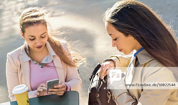 Junge erwachsene Zwillinge beim Lesen von Smartphone-Texten im Straßencafé