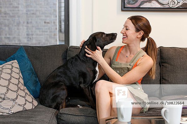 Junge Frau sitzt auf dem Sofa von Angesicht zu Angesicht mit lächelndem Hund.