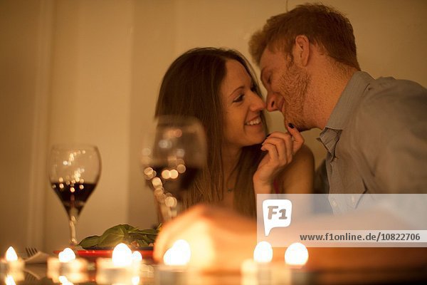 Paar genießt ein Glas Rotwein bei Kerzenlicht  von Angesicht zu Angesicht lächelnd.