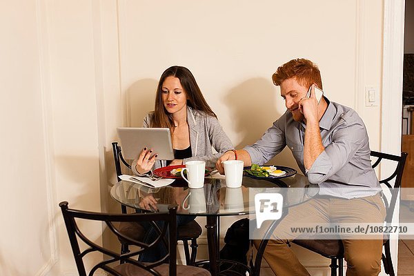 Couple at dining table using smartphone and digital tablet