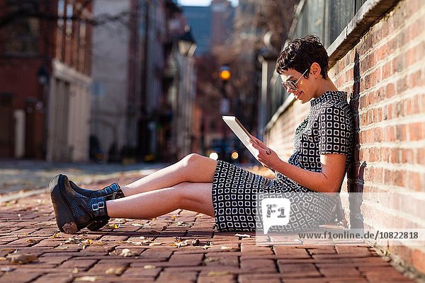 Mid adult woman sitting against brick wall  using digital tablet