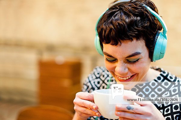 Mittlere erwachsene Frau  Kopfhörer tragend  Kaffeetasse haltend  lächelnd