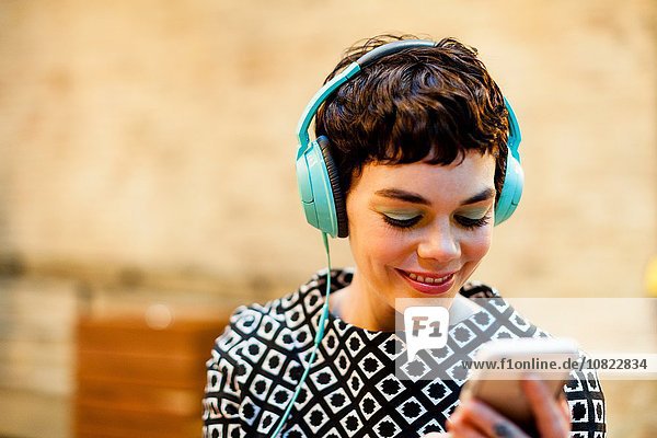 Mittlere erwachsene Frau  Kopfhörer tragend  Smartphone betrachtend  lächelnd