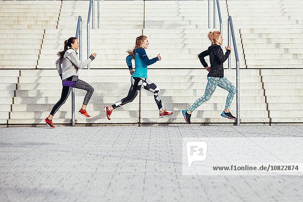 Three female runners racing past city stairway