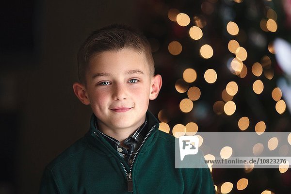 Porträt des Jungen vor dem Weihnachtsbaum mit lächelndem Blick auf die Kamera