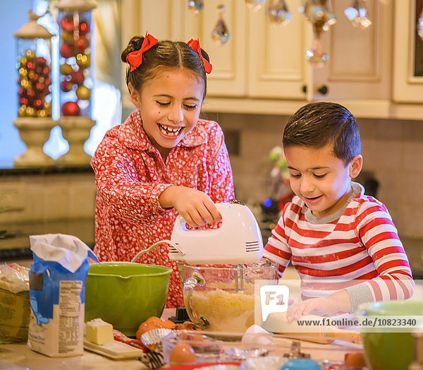 Kinder in der Küche im Pyjama mit Handmixer auf Keksteig lächelnd