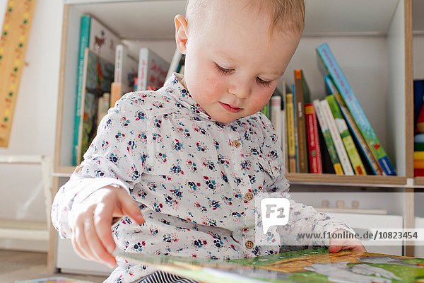 Female toddler reading book in playroom