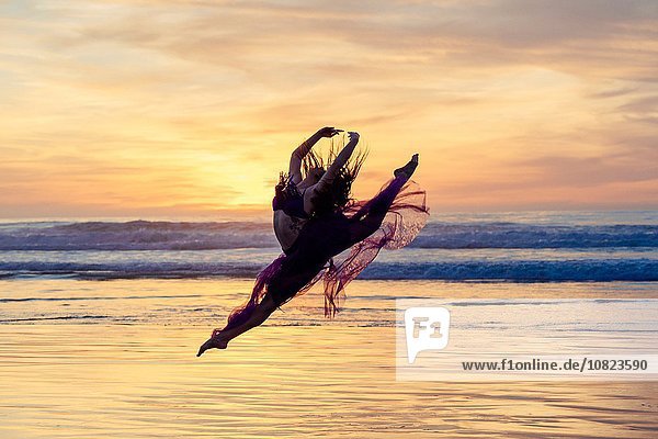 Junge Tänzerin im Chiffonkleid  tanzend  in der Luft  am Strand bei Sonnenuntergang  San Diego  Kalifornien  USA