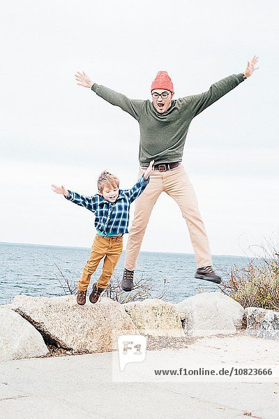 Father and son jumping off of rocks beside lake