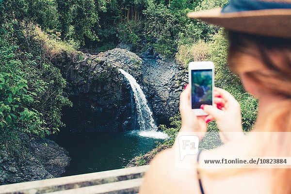 Über Schulteransicht eines weiblichen Touristen  der einen Wasserfall auf einem Smartphone fotografiert  Haleakala  Hawaii  USA