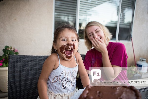 Young girl  chocolate cake on her face  sitting with family member  laughing