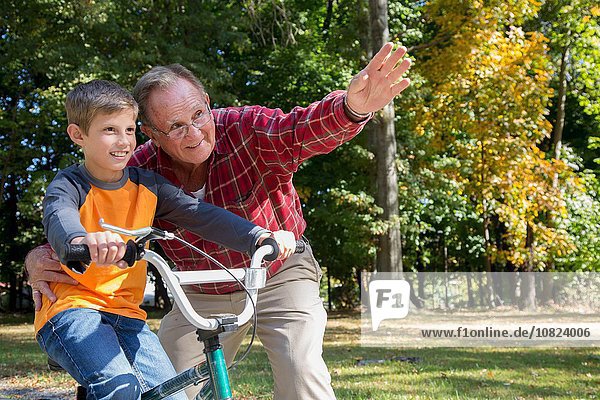 Senior man directing grandson on bicycle in woods