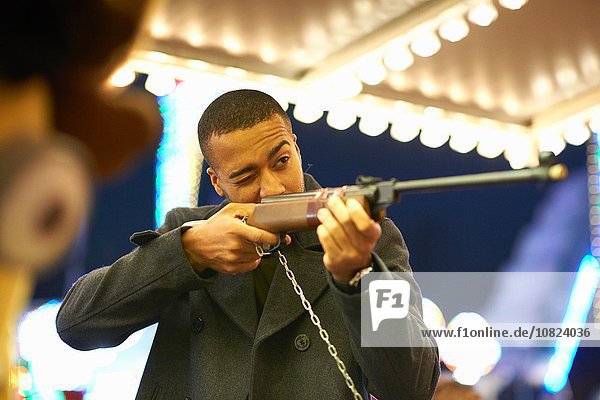 Mid adult man aiming rifle at shooting gallery at funfair