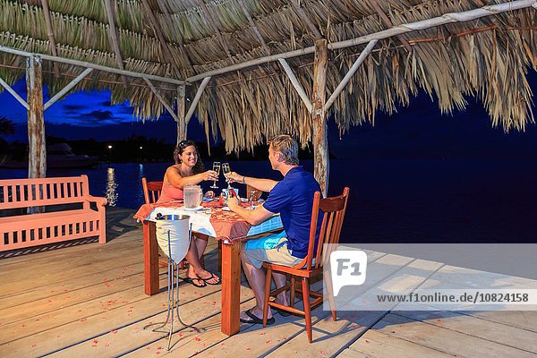 Romantisches Paar  das einen Champagner-Toast in einem Restaurant am Wasser  St. Georges Caye  Belize  Mittelamerika  ausbringt.