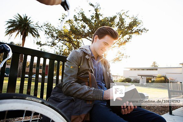 Young man reading book on sunlit park bench