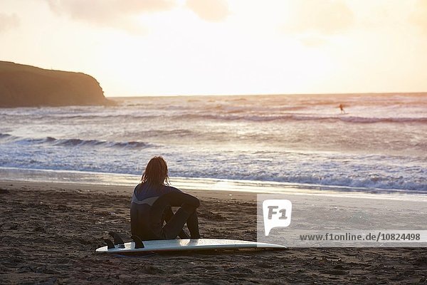 Junger Surfer sitzend mit Blick vom Strand  Devon  England  UK