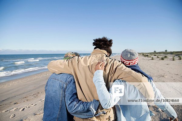 Drei Freunde gehen am Strand entlang  Arme umeinander  Rückansicht