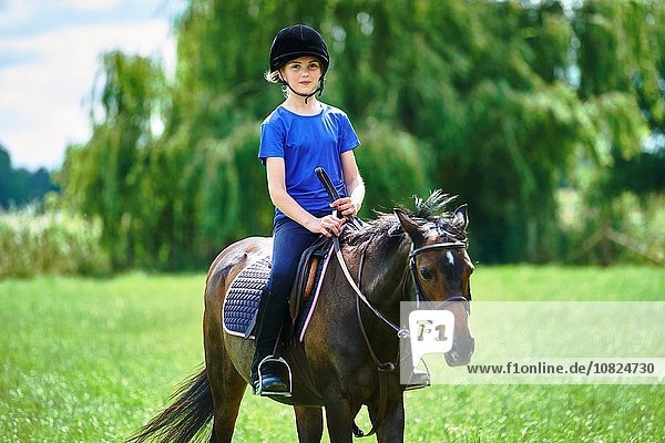 Vorderansicht des Mädchens auf dem Rücken eines Pferdes mit Reitkappe und lächelndem Blick auf die Kamera