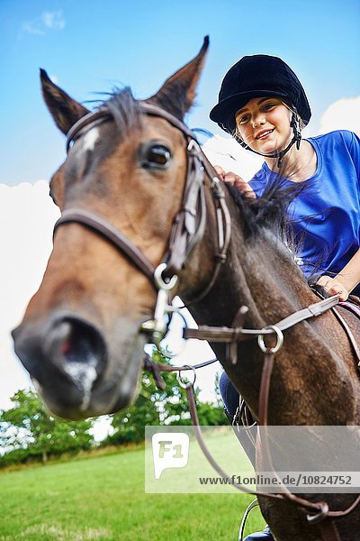 Low angle view of girl on horseback wearing riding hat smiling