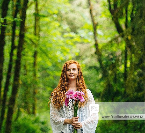 Young woman holding bunch of pink gerberas in forest
