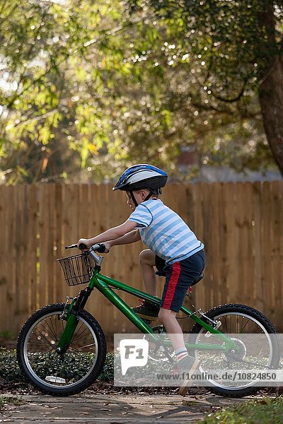 Boy riding bicycle past wooden fence