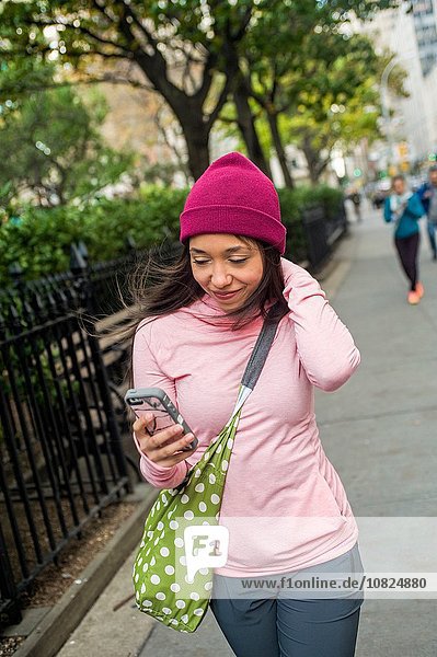 Young woman walking and using smartphone in park