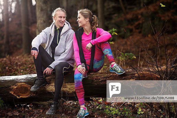 Full length view of couple wearing sports clothing sitting on fallen tree  smiling