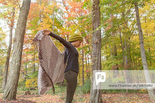 Mittlere erwachsene Frau hält ihr Tuch im Herbstwald hoch.