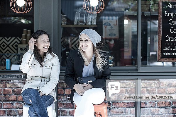 Two women friends sitting outside city cafe