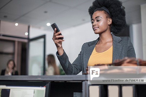 Junge Geschäftsfrau liest Smartphone-Text an der Rezeption im Büro