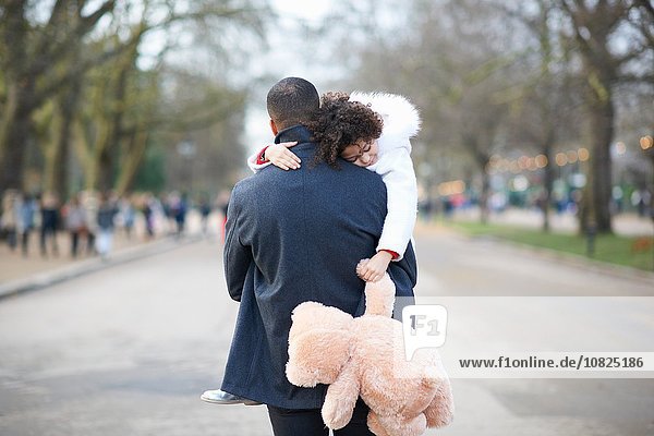 Rear view of father carrying sleeping daughter holding cuddly toy