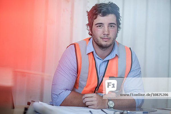 Portrait of young male construction worker sitting at desk in portable cabin